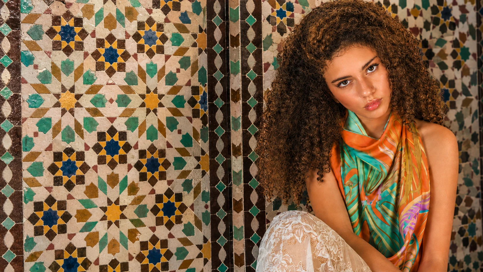 Foulard di seta NinaMoire arancio e turchese annodato al collo, davanti allo zellige